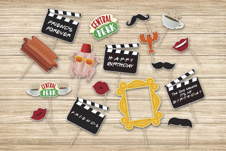 May include: A collection of Friends-themed photo booth props on sticks, including a brown sofa, Central Perk signs, black clapperboards with text, a turkey with a fez and sunglasses, a yellow picture frame, a lobster, coffee cups, and mustaches.