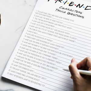 K&ouml;nnte beinhalten: Ein druckbares Quizspiel mit 23 Fragen &uuml;ber die beliebte Fernsehserie "Friends". Die Fragen sind in schwarzer Tinte auf einem wei&szlig;en Blatt Papier geschrieben. Das Papier liegt auf einer wei&szlig;en Marmorfl&auml;che.