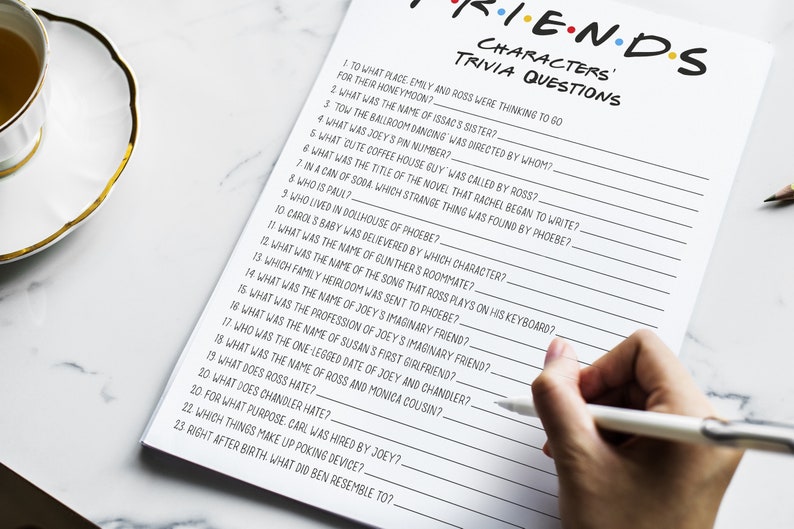 K&ouml;nnte beinhalten: Ein druckbares Quizspiel mit 23 Fragen &uuml;ber die beliebte Fernsehserie "Friends". Die Fragen sind in schwarzer Tinte auf einem wei&szlig;en Blatt Papier geschrieben. Das Papier liegt auf einer wei&szlig;en Marmorfl&auml;che.