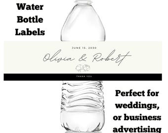 May include: Clear water bottle with a custom label. The label is cream-colored with black text that reads "Olivia & Robert" and "June 15, 2030". The words "Custom Water Bottle Labels" are at the top.