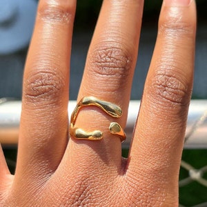 Peut inclure: Une bague en or avec une forme abstraite et organique. La bague est portée sur le majeur d'une main.