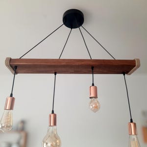 Op de afbeelding: Een rustieke houten plafondlamp met vier koperkleurige lampen en zwarte snoeren.