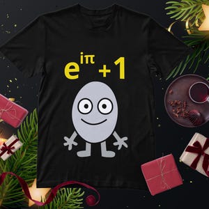 May include: Black t-shirt with a cartoon egg character and the mathematical formula "e^iπ + 1" in yellow. The egg has a smiling face, arms, and legs. The image is decorated with festive elements.