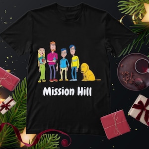 May include: Black t-shirt with a cartoon image of five characters, a dog, and the text "Mission Hill" in white. The characters are in different outfits, and the dog is yellow. The shirt is surrounded by festive decorations.