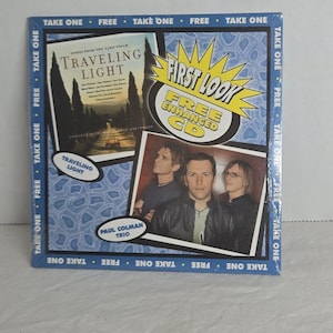 May include: A CD case with the album title "Traveling Light" and the Paul Colman Trio. The cover features a photo of the band and a landscape image. The case has a blue border with the words "Take One" and "Free".
