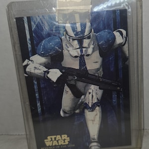May include: A Star Wars trading card featuring a clone trooper in white and blue armor, holding a blaster. The card is from "Revenge of the Sith" and is encased in a protective sleeve.