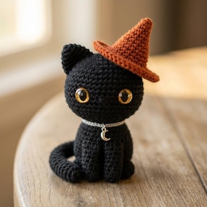 May include: A crocheted black cat figurine wearing an orange witch hat and a silver collar with a crescent moon charm. The cat has large, golden eyes and is sitting upright. The cat is on a wooden surface.