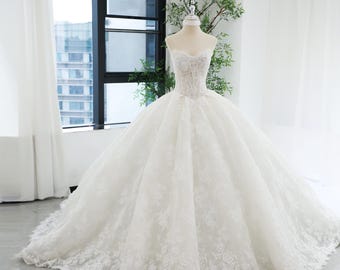 Vestido de novia de encaje blanco: vestido vasco con escote en forma de corazón, cola estilo catedral y pedrería abundante.