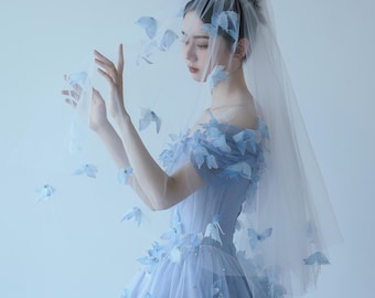 May include: A light blue tulle wedding dress with off-the-shoulder sleeves, adorned with delicate blue floral appliqués. A sheer veil with matching floral accents completes the bridal ensemble. The dress features a fitted bodice and a flowing skirt.
