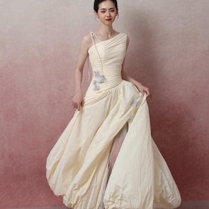 Può includere: Un abito color crema monospalla con corpetto drappeggiato e gonna ampia. L'abito presenta una vita arricciata e una gonna fluida e voluminosa. Il tessuto sembra leggero e l'abito ha un'estetica delicata e femminile. L'abito è adatto per eventi formali.