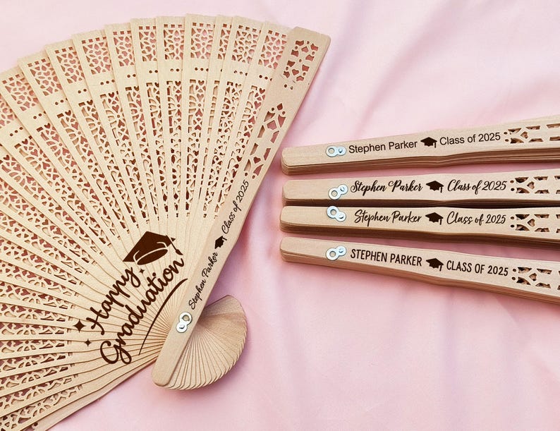 May include: Wooden graduation fans with intricate cut-out designs. One fan is open, displaying "Happy Graduation" and a graduation cap graphic. The handles of the fans are engraved with "Stephen Parker Class of 2025".