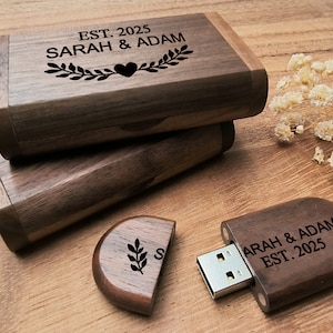 May include: A wooden USB flash drive with a personalized inscription: "SARAH & ADAM EST. 2025". The drive is in the shape of a rectangle with rounded edges and has a dark brown finish. The inscription is engraved in a white font. The drive is accompanied by a wooden box with a similar inscription and design.
