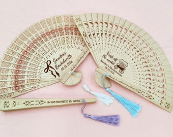 May include: Wooden fans with intricate cut-out designs, featuring floral and geometric patterns. One fan has the text "Sandra's Bachelorette 08.14.2026". Another fan has the text "Fresh off the market Sandra's Bachelorette 08.14.2026". Each fan has a tassel.