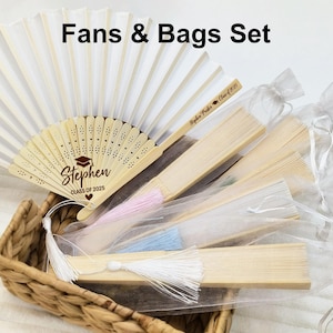 May include: A set of white hand fans with personalized wooden handles and white organza bags. The fans have a white paper surface and a wooden handle with the text "Stephen Class of 2025" printed on it. The bags are made of sheer white organza fabric and have a drawstring closure.