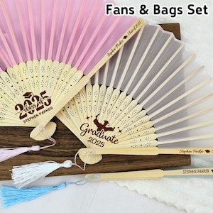 May include: Two personalized hand fans with tassels. The fans are made of bamboo and have a white silk fabric. One fan has the text "Graduate 2025" and the other has the text "Class of 2025 Stephen Parker".