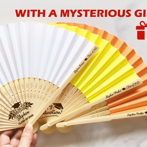 May include: Three hand fans with bamboo handles and paper panels in white, yellow, and orange. The fans are decorated with the text "Stephen Parker Class of 2025" and a graduation cap graphic. The white fan has a floral design and the text "Stephen Class of 2025".