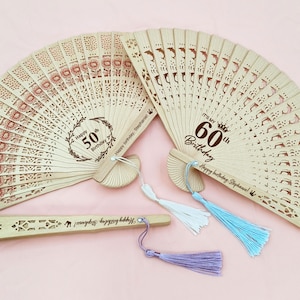 Op de afbeelding: Twee houten vouwvaandels met decoratieve uitsnijdingen en kwastjes. De grotere waaier heeft de tekst "It's my 60th Birthday" en "Happy birthday, Stephanie!" De kleinere waaier heeft de tekst "Happy 50th Birthday" en "Happy birthday, Stephanie!"