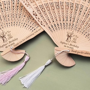 May include: Two wooden hand fans with a laser-engraved design of a cocktail glass and the text "A Tini Bit Older" and "Sophia's Birthday 09.18.2025" and "Thank you for celebrating with me!"
