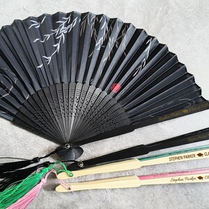 May include: Three black folding fans with gold lettering. The fans have black handles with tassels. The lettering on the fans reads "Stephen Parker Class of 2025".