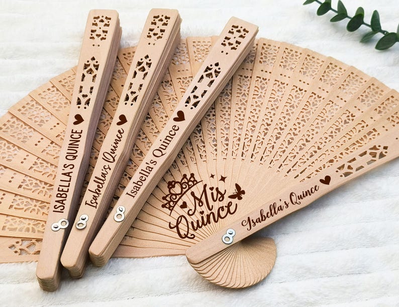 Puede incluir: Cuatro abanicos de mano de madera con un dise&ntilde;o de encaje y el texto "Isabella's Quince" y "Mis Quince" en letras marrones.