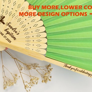 May include: A personalized wooden fan with a green paper backing. The fan is engraved with a cross, the words "Sandra's baptism," and the date June 27, 2025. The handle reads "Thank you for celebrating for us."
