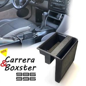 May include: Black plastic storage organizer for a Porsche 911 Carrera or Boxster. The organizer fits in the center console and has two compartments. The organizer is shown in a car interior.