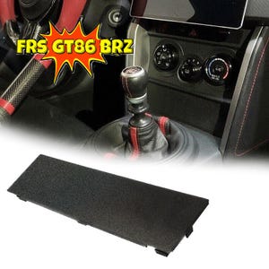 May include: Black plastic trim piece for a car interior. The trim piece is textured and has a rectangular shape. It is designed to fit in the center console of a car.