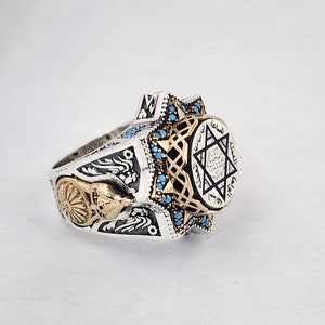 May include: A silver ring with a gold Star of David design and blue turquoise stones. The ring features Arabic text around the star.