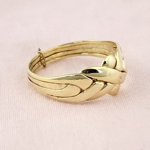 Op de afbeelding: Een gouden puzzelring met een uniek, in elkaar grijpend ontwerp. De ring is gemaakt van meerdere banden die met elkaar zijn verweven.