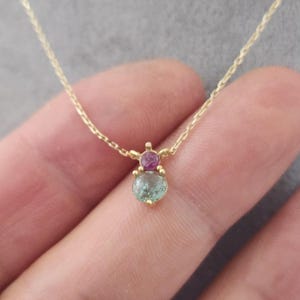 Puede incluir: Un delicado collar de cadena de oro con un colgante que presenta una piedra preciosa redonda verde y una piedra preciosa rosa más pequeña.