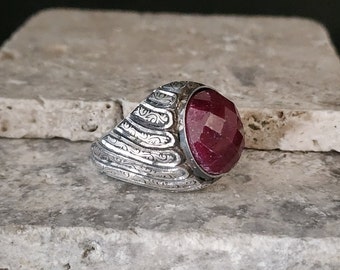 May include: A silver ring with an ornate design and a large, faceted ruby gemstone.