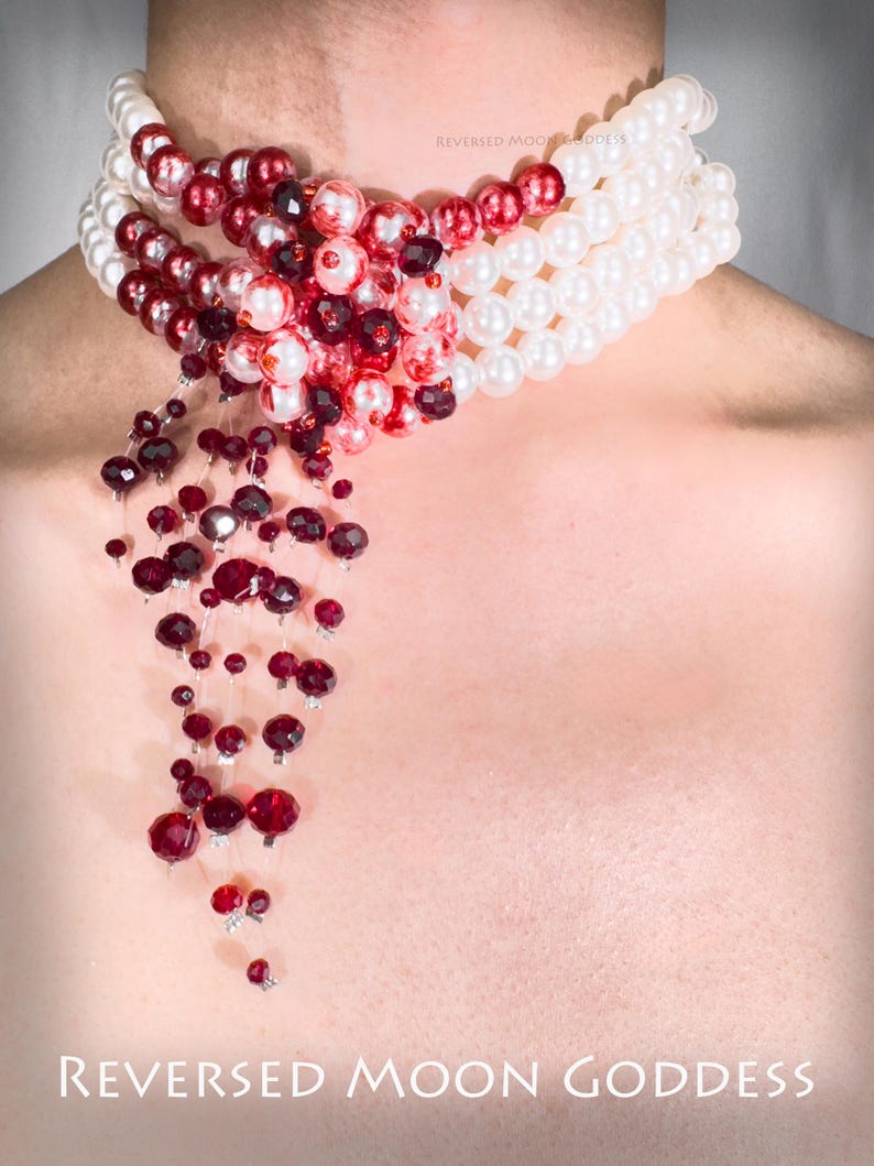 Puede incluir: Un collar de varias capas con cuentas blancas y rojas. El collar tiene un dise&ntilde;o en cascada con cuentas de cristal rojas que cuelgan de la parte inferior. El texto "REVERSED MOON GODDESS" est&aacute; impreso en la parte inferior de la imagen.
