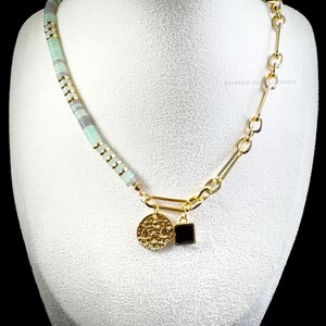 May include: A gold chain necklace with a green and grey beaded strand, a gold coin pendant with a symbol, and a black square pendant. The necklace is displayed on a white mannequin. The text "REVERSED MOON GODDESS" is visible at the bottom of the image.