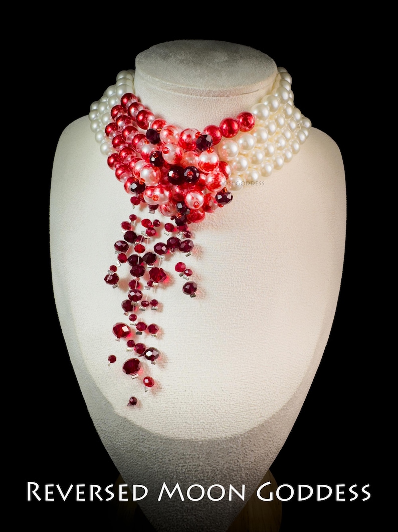 Puede incluir: Un collar de cuentas rojas y blancas con un dise&ntilde;o en cascada. El collar est&aacute; hecho de cuentas rojas y blancas y tiene un dise&ntilde;o largo y fluido. El collar est&aacute; en un maniqu&iacute; blanco.