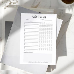 K&ouml;nnte beinhalten: Ein wei&szlig;es Habit-Tracker-Blatt mit dem Titel "Habit Tracker" in handschriftlicher Schrift. Das Blatt hat Platz f&uuml;r Daten, Gewohnheiten und Kontrollk&auml;stchen f&uuml;r jeden Wochentag. Eine Tasse Kaffee steht in der N&auml;he.