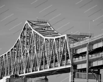 May include: A black and white photograph of a large steel bridge with a complex truss design. The bridge is made up of many interconnected triangles and beams.
