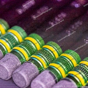 May include: Close-up of a row of green and yellow pencils with gray erasers. The pencils are arranged in a row, with the erasers facing the viewer. The pencils are all the same size and shape, and they have a green and yellow striped pattern.
