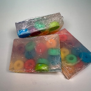 Puede incluir: Tres barras de jabón transparentes con círculos coloridos incrustados. Las barras de jabón están envueltas en plástico transparente.