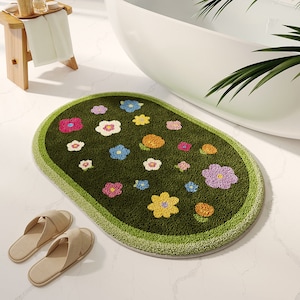 Puede incluir: Una alfombra de baño ovalada con fondo verde y diseños de flores de colores. La alfombra tiene un borde verde claro.