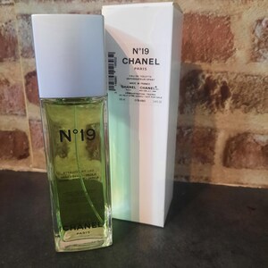 Pu&ograve; includere: Un flacone rettangolare in vetro di Chanel N&deg;19 Eau de Toilette con tappo bianco e liquido verde chiaro, accompagnato dalla sua scatola di cartone bianca. Il flacone e la scatola riportano il marchio Chanel N&deg;19 e indicano un volume di 100 ml.