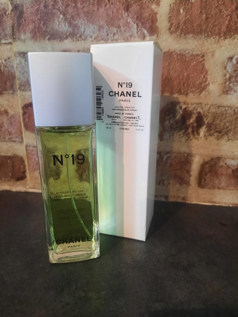 Pu&ograve; includere: Un flacone rettangolare in vetro di Chanel N&deg;19 Eau de Toilette con tappo bianco e liquido verde chiaro, accompagnato dalla sua scatola di cartone bianca. Il flacone e la scatola riportano il marchio Chanel N&deg;19 e indicano un volume di 100 ml.