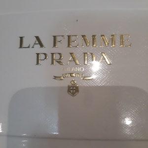 Peut inclure: Une boîte blanche avec des lettres dorées qui lisent "La Femme Prada Milano 1913" avec un logo d'ancre dorée. La boîte indique également "Eau de Parfum Vaporisateur Spray e 35ml 1.2 FL OZ".