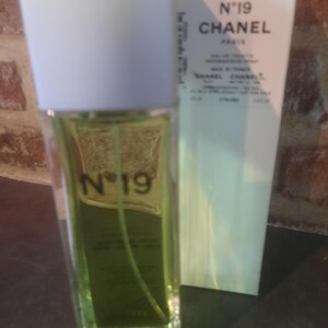 Pu&ograve; includere: Un flacone rettangolare in vetro di eau de toilette Chanel N&deg;19 contenente un liquido verde chiaro, con tappo bianco e scritte nere. Accanto si trova una scatola rettangolare bianca alta con la scritta N&deg;19 CHANEL PARIS stampata in nero.