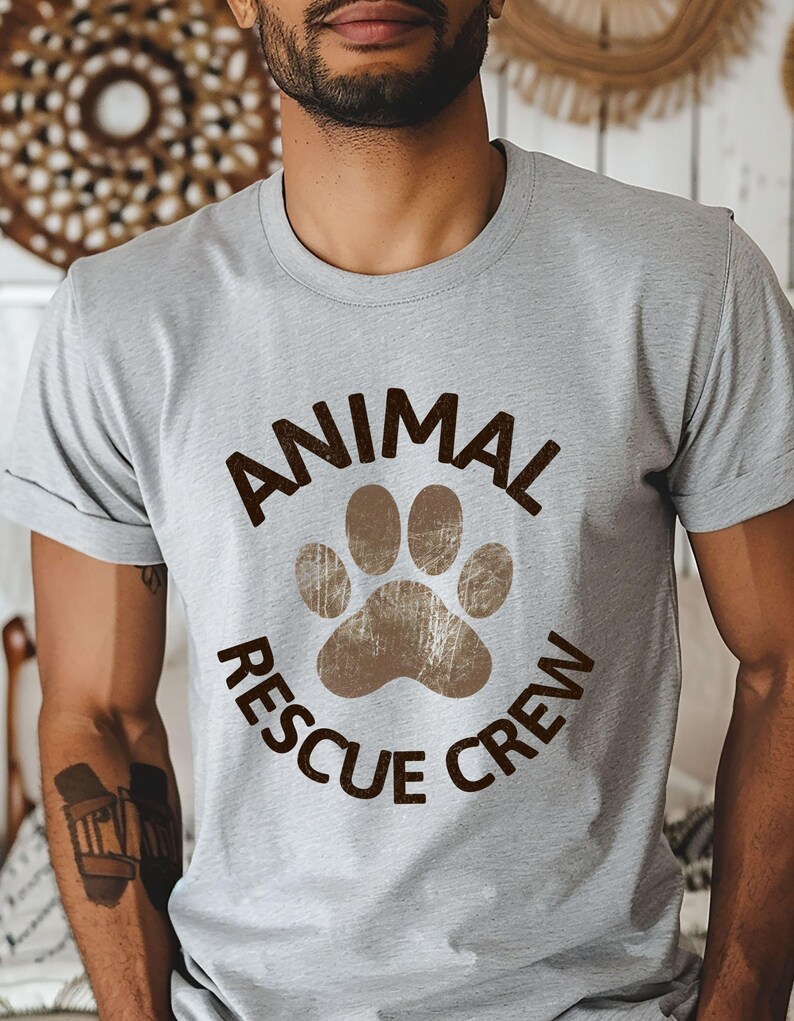 May include: A light gray t-shirt with the words "ANIMAL RESCUE CREW" in brown, encircling a brown paw print. The shirt is short-sleeved and has a crew neck.