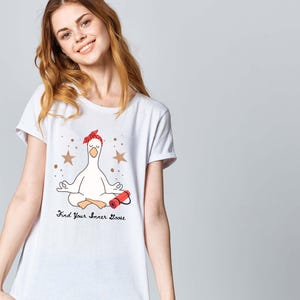 May include: White t-shirt with a cartoon goose in a yoga pose, wearing a red bandana and holding a red object. The shirt has the text "Find Your Inner Goose" with star accents.