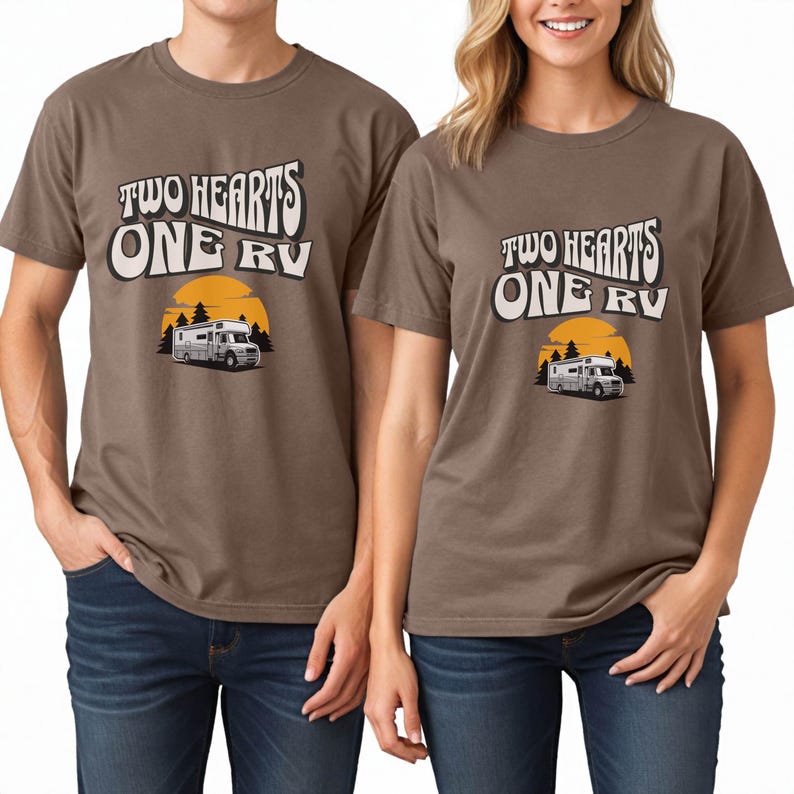 Pu&ograve; includere: Due magliette marroni con la scritta "TWO HEARTS ONE RV" in un font retr&ograve;. Il design include una grafica di un camper davanti a un tramonto giallo e pini. Le magliette sono indossate da due persone.