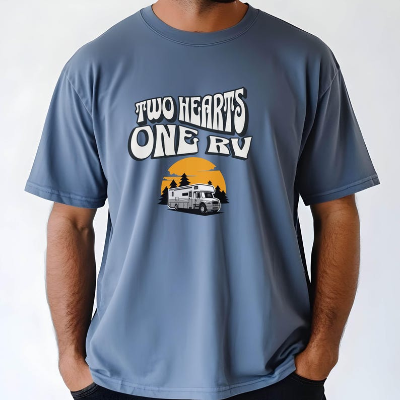 Pu&ograve; includere: T-shirt blu con la scritta "TWO HEARTS ONE RV" in un font retr&ograve;. Sotto il testo c'&egrave; una grafica di un camper davanti a un tramonto e alberi. La maglietta &egrave; di colore blu unito.
