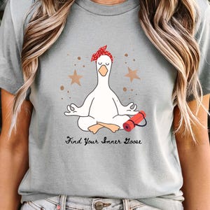 May include: A light grey t-shirt with a cartoon goose meditating, wearing a red polka dot headband. A red yoga mat is beside the goose. The text "Find Your Inner Goose" is below the goose.