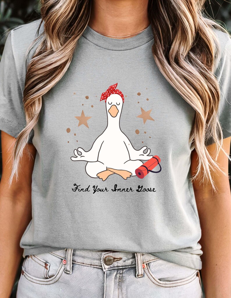 May include: A light grey t-shirt with a cartoon goose meditating, wearing a red polka dot headband. A red yoga mat is beside the goose. The text "Find Your Inner Goose" is below the goose.