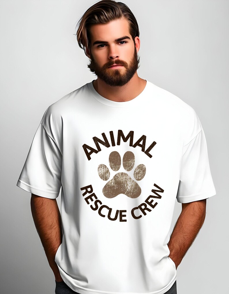 May include: White t-shirt with a brown paw print and the words "ANIMAL RESCUE CREW" in a circular design. The shirt has short sleeves and a relaxed fit.